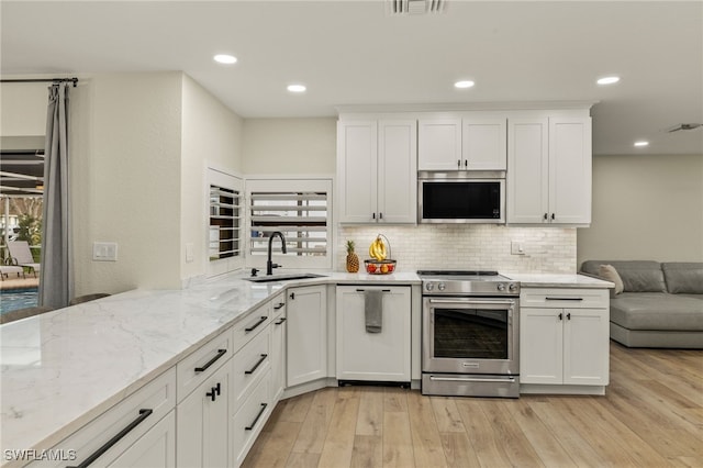 kitchen with light stone counters, light wood finished floors, decorative backsplash, appliances with stainless steel finishes, and a sink