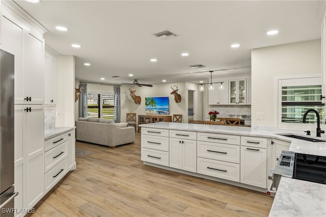 kitchen featuring light wood-style floors, open floor plan, white cabinets, a sink, and a peninsula