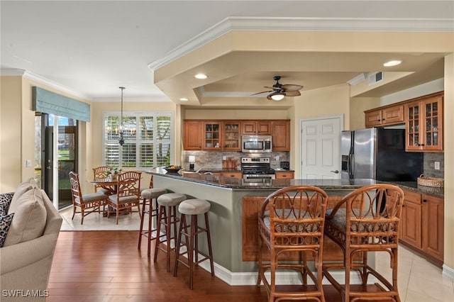 kitchen featuring glass insert cabinets, appliances with stainless steel finishes, brown cabinets, a kitchen bar, and pendant lighting