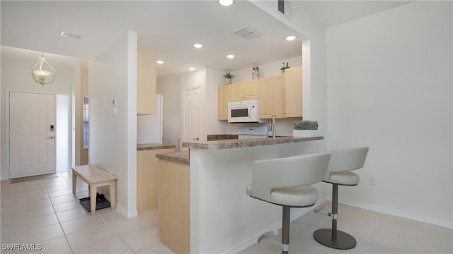 kitchen featuring light tile patterned floors, white microwave, a breakfast bar area, recessed lighting, and light brown cabinetry