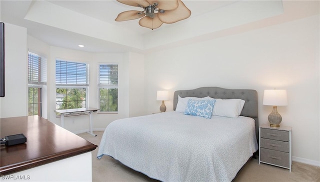 bedroom with a ceiling fan, a tray ceiling, light colored carpet, and baseboards