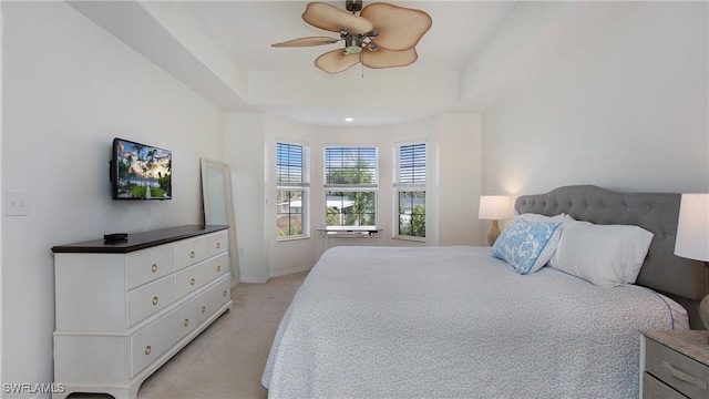 bedroom with a ceiling fan, a raised ceiling, light carpet, and baseboards