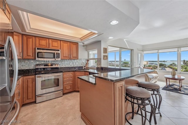 kitchen featuring appliances with stainless steel finishes, brown cabinets, a raised ceiling, and dark stone countertops