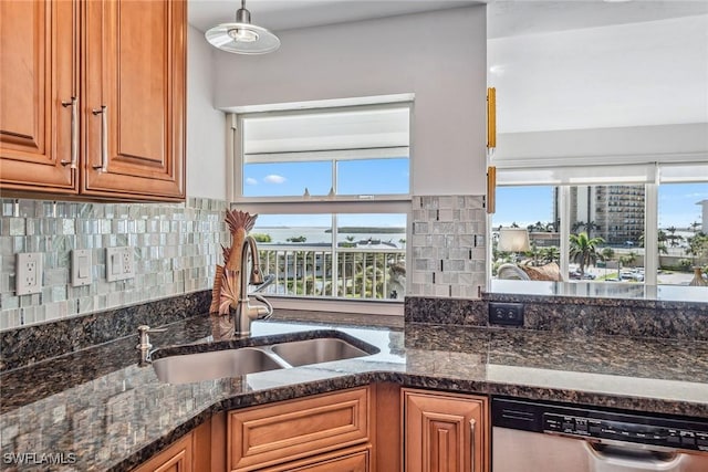 kitchen featuring a sink, hanging light fixtures, decorative backsplash, brown cabinetry, and stainless steel dishwasher