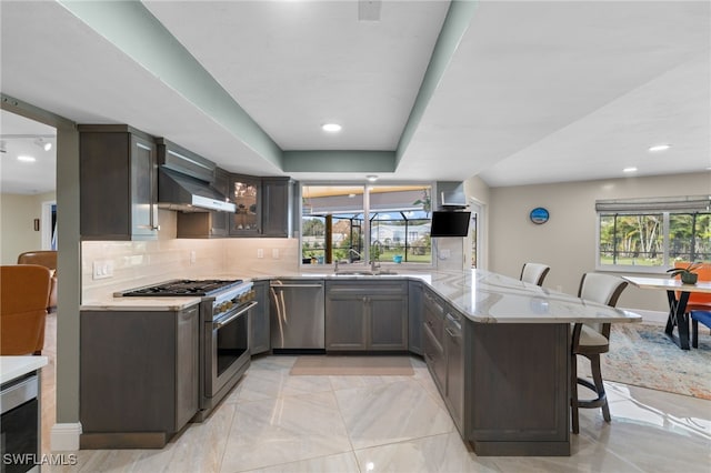 kitchen featuring a peninsula, a kitchen breakfast bar, appliances with stainless steel finishes, wall chimney range hood, and tasteful backsplash