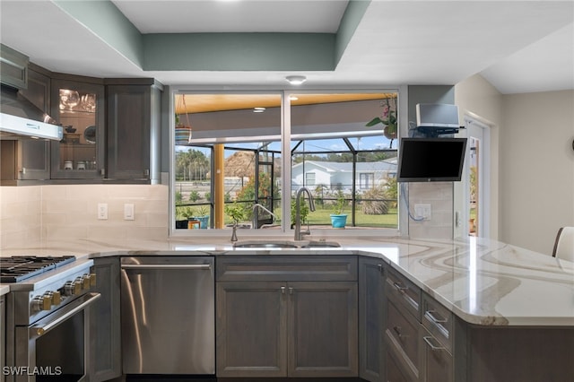 kitchen featuring stainless steel appliances, tasteful backsplash, a sink, light stone countertops, and a peninsula