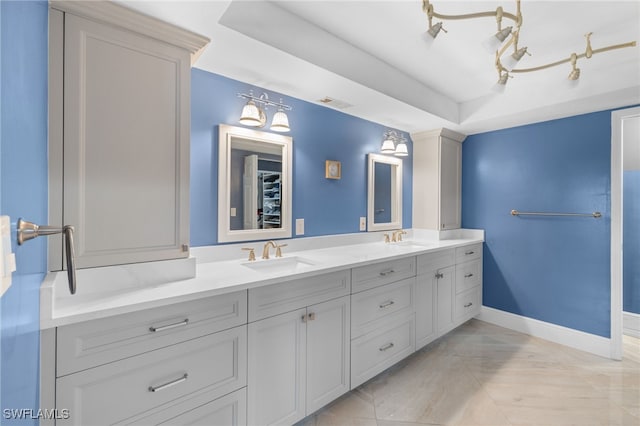 full bathroom with a tray ceiling, a sink, baseboards, and double vanity