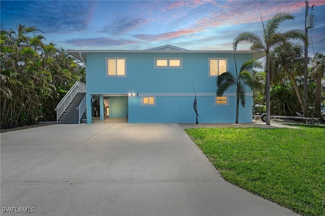 coastal home with a front yard, concrete driveway, stairway, and stucco siding