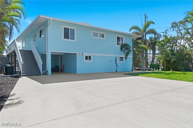 exterior space featuring central air condition unit, stairs, concrete driveway, stucco siding, and a carport