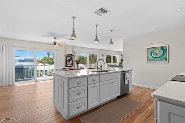 kitchen with a center island with sink, visible vents, hanging light fixtures, light wood-style floors, and a sink