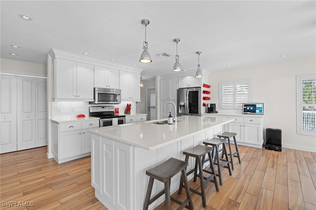 kitchen with stainless steel appliances, light countertops, a kitchen island with sink, and white cabinetry