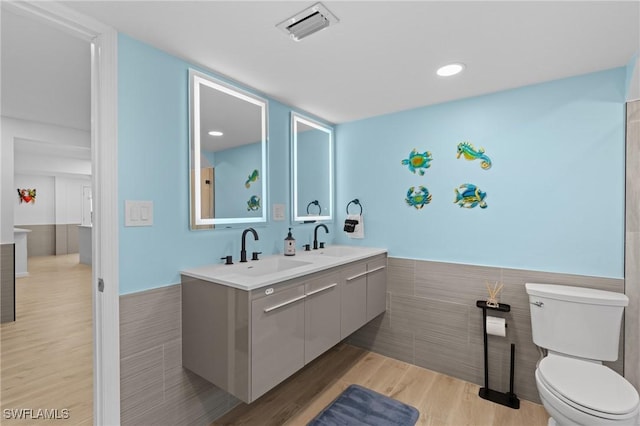 full bathroom with wood finished floors, visible vents, a sink, and double vanity