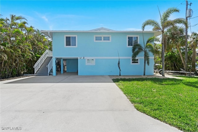 beach home with driveway, stucco siding, stairway, a carport, and a front yard