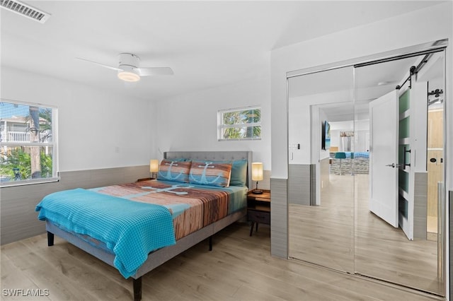 bedroom with a barn door, visible vents, a ceiling fan, wainscoting, and light wood-style flooring