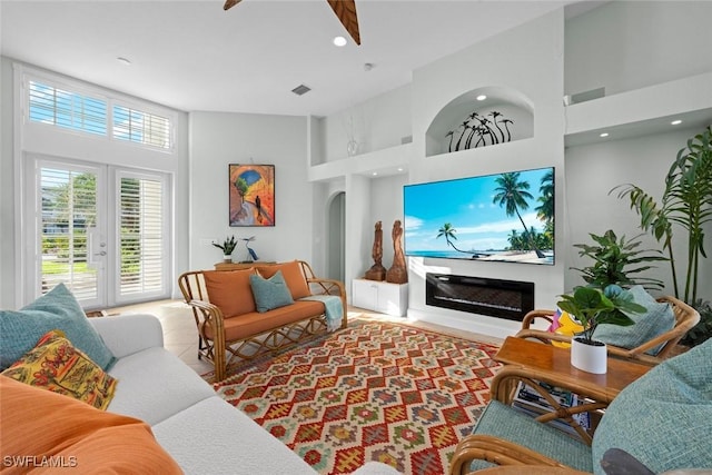 tiled living area featuring a high ceiling, arched walkways, a wealth of natural light, and a glass covered fireplace