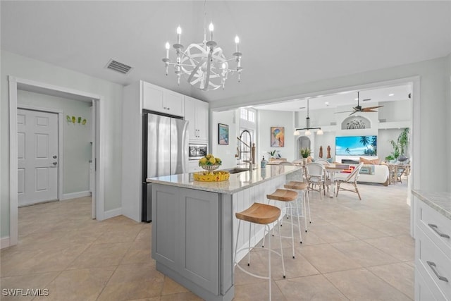 kitchen featuring a sink, white cabinets, freestanding refrigerator, light stone countertops, and an island with sink