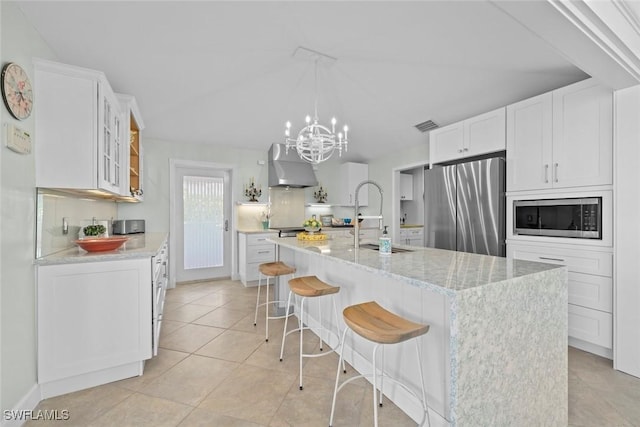 kitchen featuring stainless steel appliances, white cabinetry, a center island with sink, and wall chimney exhaust hood