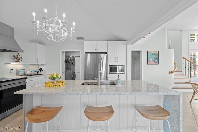 kitchen featuring stainless steel appliances, stacked washer and dryer, a kitchen bar, and white cabinets