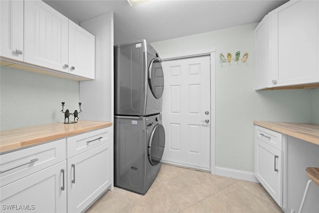 laundry room featuring stacked washer and clothes dryer, cabinet space, baseboards, and light tile patterned floors