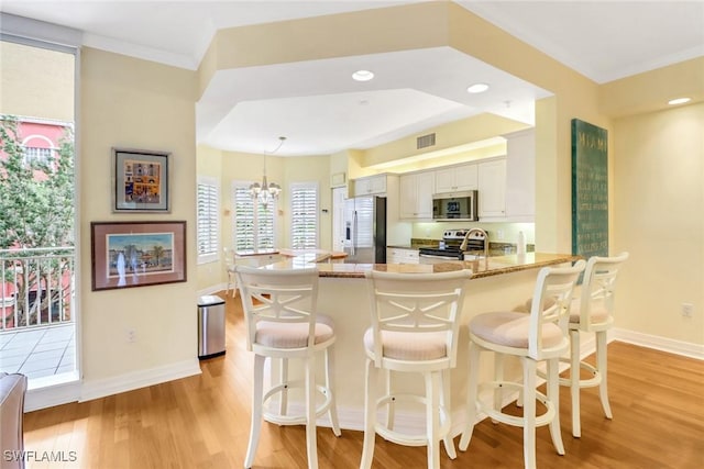 kitchen with a peninsula, baseboards, appliances with stainless steel finishes, light wood-type flooring, and a kitchen bar