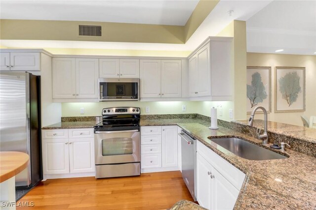 kitchen featuring stone counters, stainless steel appliances, visible vents, light wood-style flooring, and a sink