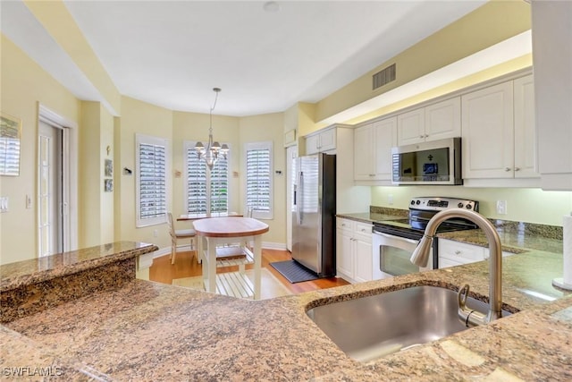 kitchen with visible vents, appliances with stainless steel finishes, hanging light fixtures, stone counters, and a sink