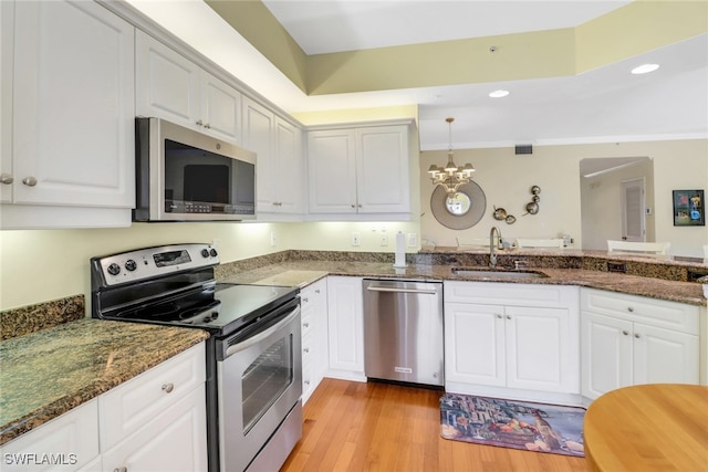 kitchen with light wood-style flooring, an inviting chandelier, appliances with stainless steel finishes, white cabinets, and a sink