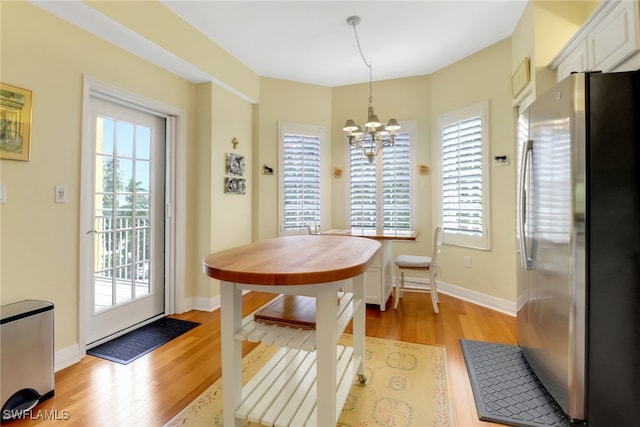 dining space featuring light wood-type flooring, a wealth of natural light, baseboards, and an inviting chandelier