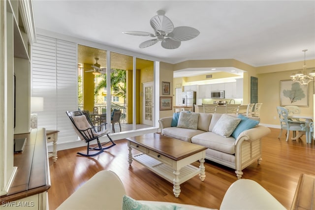 living area featuring ceiling fan with notable chandelier, baseboards, expansive windows, and wood finished floors