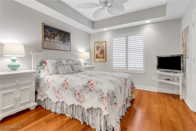 bedroom with light wood-style floors, ceiling fan, baseboards, and a raised ceiling