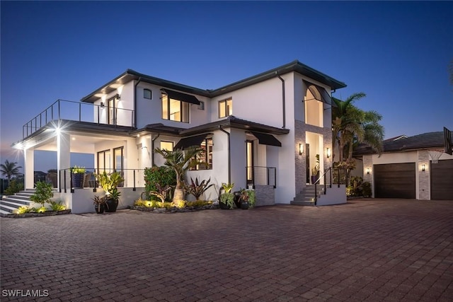 view of front of property with decorative driveway, an attached garage, a balcony, and stucco siding