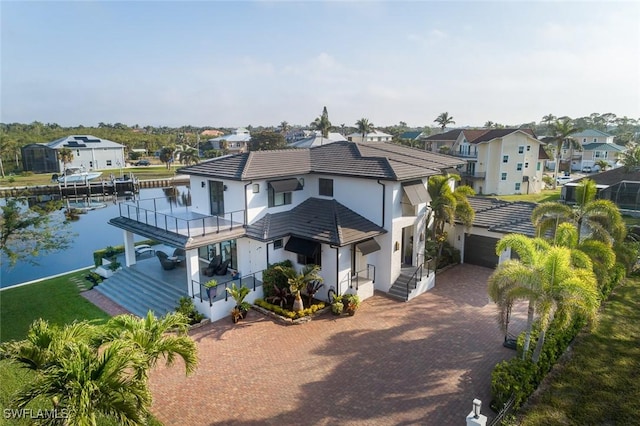 view of front facade with an attached garage, a balcony, a water view, decorative driveway, and a residential view