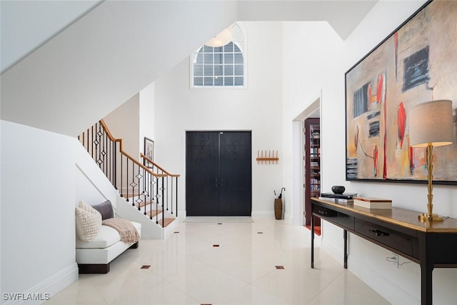 tiled foyer entrance featuring a high ceiling, stairway, and baseboards