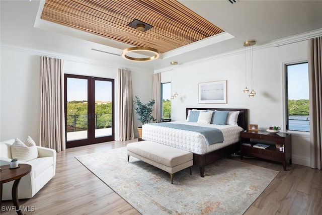 bedroom with light wood-type flooring, a tray ceiling, crown molding, and french doors