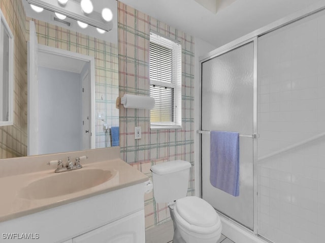 bathroom with a stall shower, vanity, toilet, and wallpapered walls