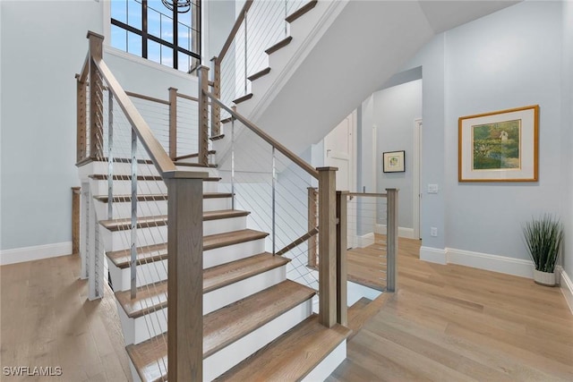 stairway featuring a high ceiling, baseboards, and wood finished floors