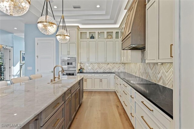 kitchen with premium range hood, light wood finished floors, pendant lighting, a raised ceiling, and black electric stovetop