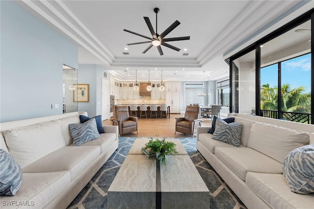 living area with recessed lighting, crown molding, a tray ceiling, and wood finished floors