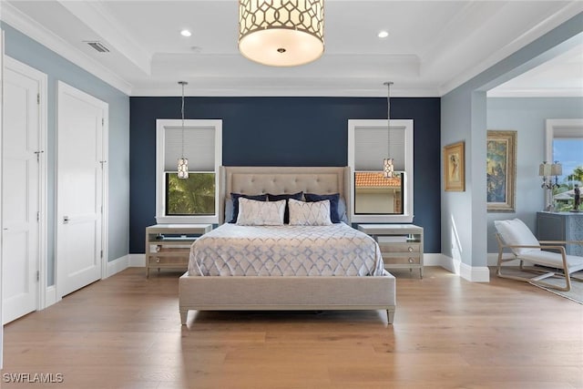 bedroom with a tray ceiling, wood finished floors, visible vents, and ornamental molding