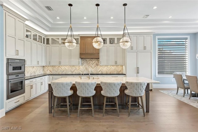 kitchen featuring decorative backsplash, an island with sink, light wood-style floors, and visible vents