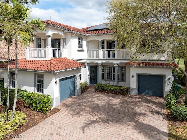 mediterranean / spanish-style house featuring solar panels, a tiled roof, a balcony, and stucco siding