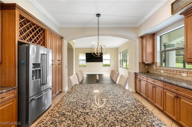 kitchen featuring tasteful backsplash, high end refrigerator, dark stone countertops, crown molding, and pendant lighting