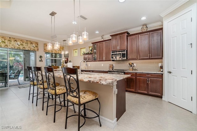 kitchen featuring light stone counters, a kitchen island with sink, a kitchen breakfast bar, hanging light fixtures, and appliances with stainless steel finishes