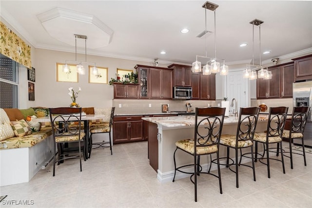 kitchen with a breakfast bar, crown molding, stainless steel appliances, hanging light fixtures, and an island with sink