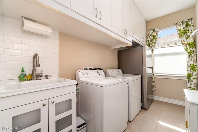 washroom featuring light tile patterned floors, cabinet space, a sink, separate washer and dryer, and baseboards