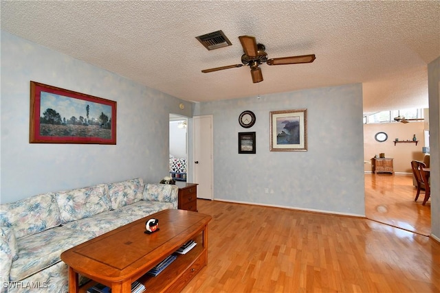 living room with baseboards, visible vents, a ceiling fan, light wood-style flooring, and a textured ceiling