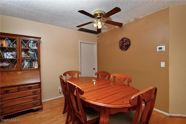 dining space with light wood-type flooring, ceiling fan, baseboards, and a textured ceiling