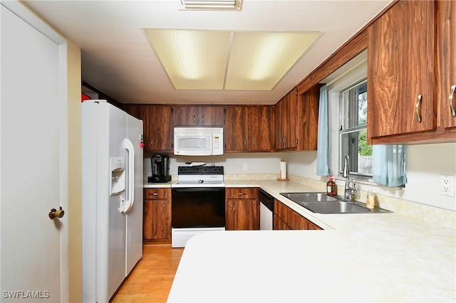 kitchen with brown cabinetry, white appliances, light countertops, and a sink