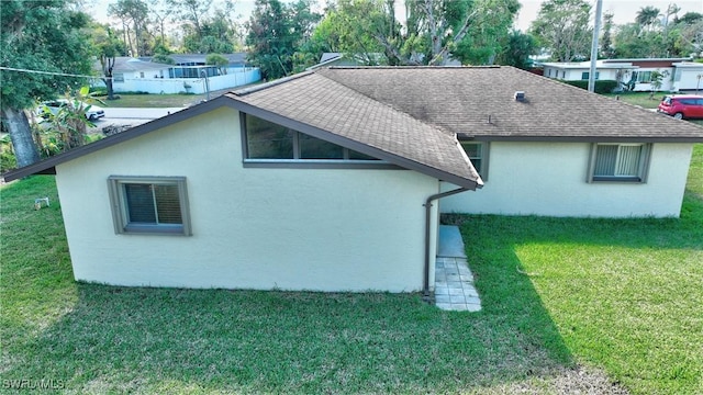 view of home's exterior with roof with shingles, a yard, and stucco siding