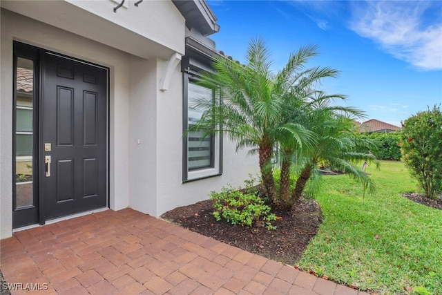 property entrance featuring a lawn and stucco siding